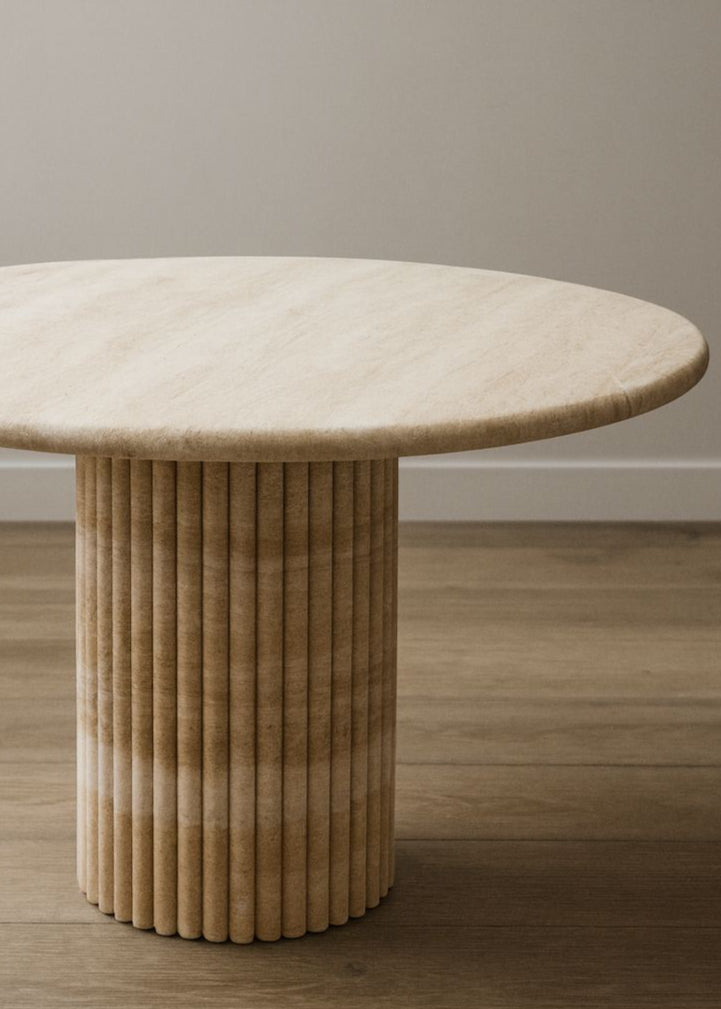 Round Travertine table with a ribbed cylindrical base on a wooden floor.